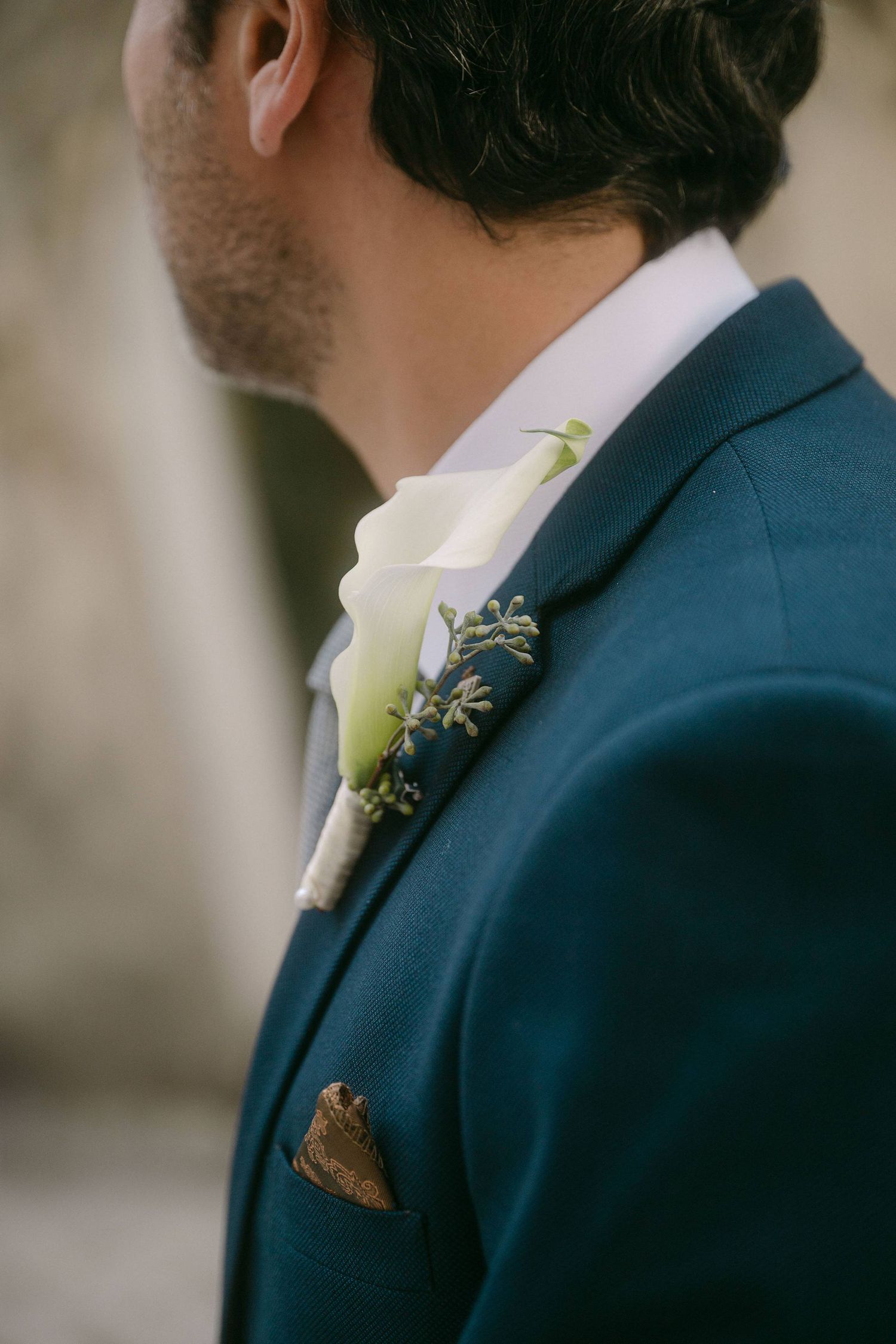 Close-up detail of navy blue suit jacket with white boutonniere flower pinned to lapel.