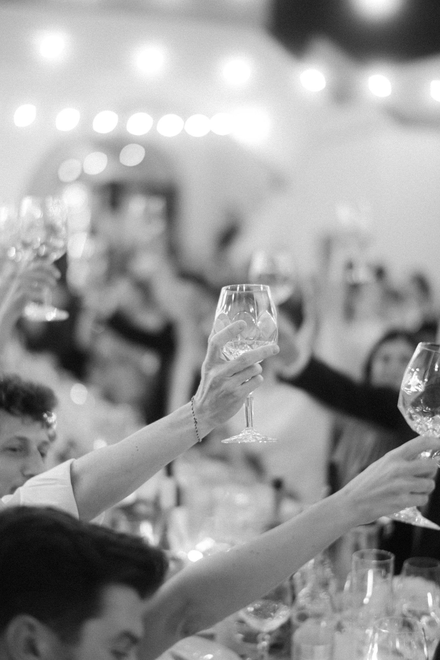Multiple raised wine glasses in a celebratory toast at an elegant event with blurred background lighting.