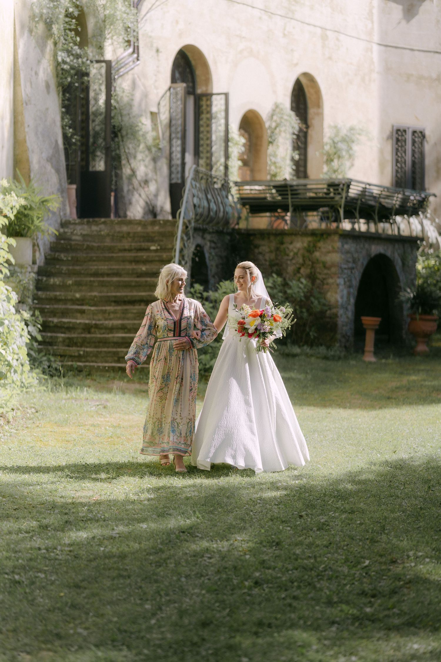 A sequence of outdoor wedding photos showing a couple walking together on a grassy lawn near a historic stone building.