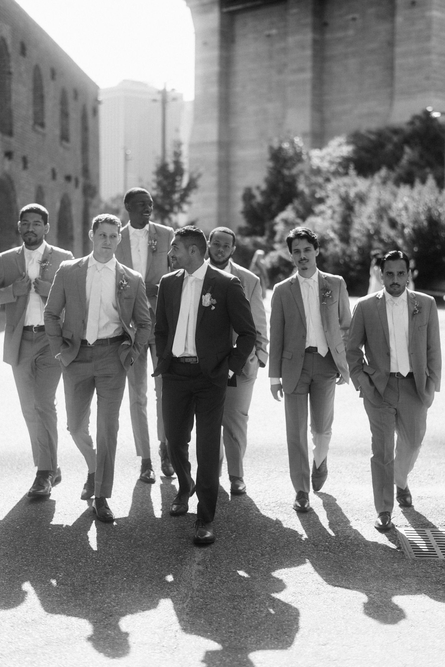 A group of men in suits walking together casting long shadows on a sunlit street in black and white photography.