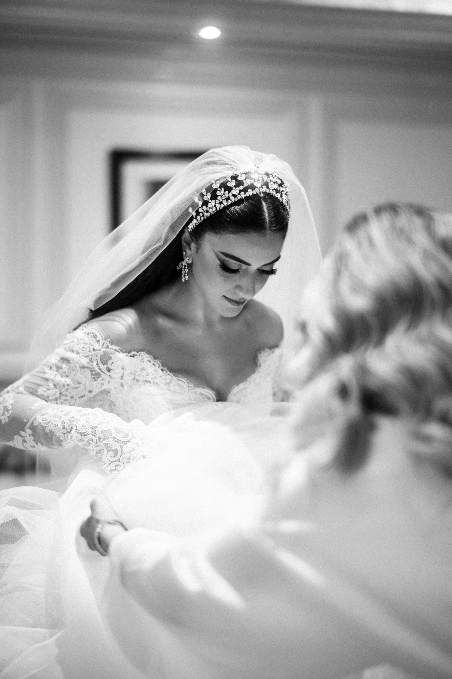 Beautiful black and white wedding photo showing bride getting ready in lace dress with ornate tiara and long veil.