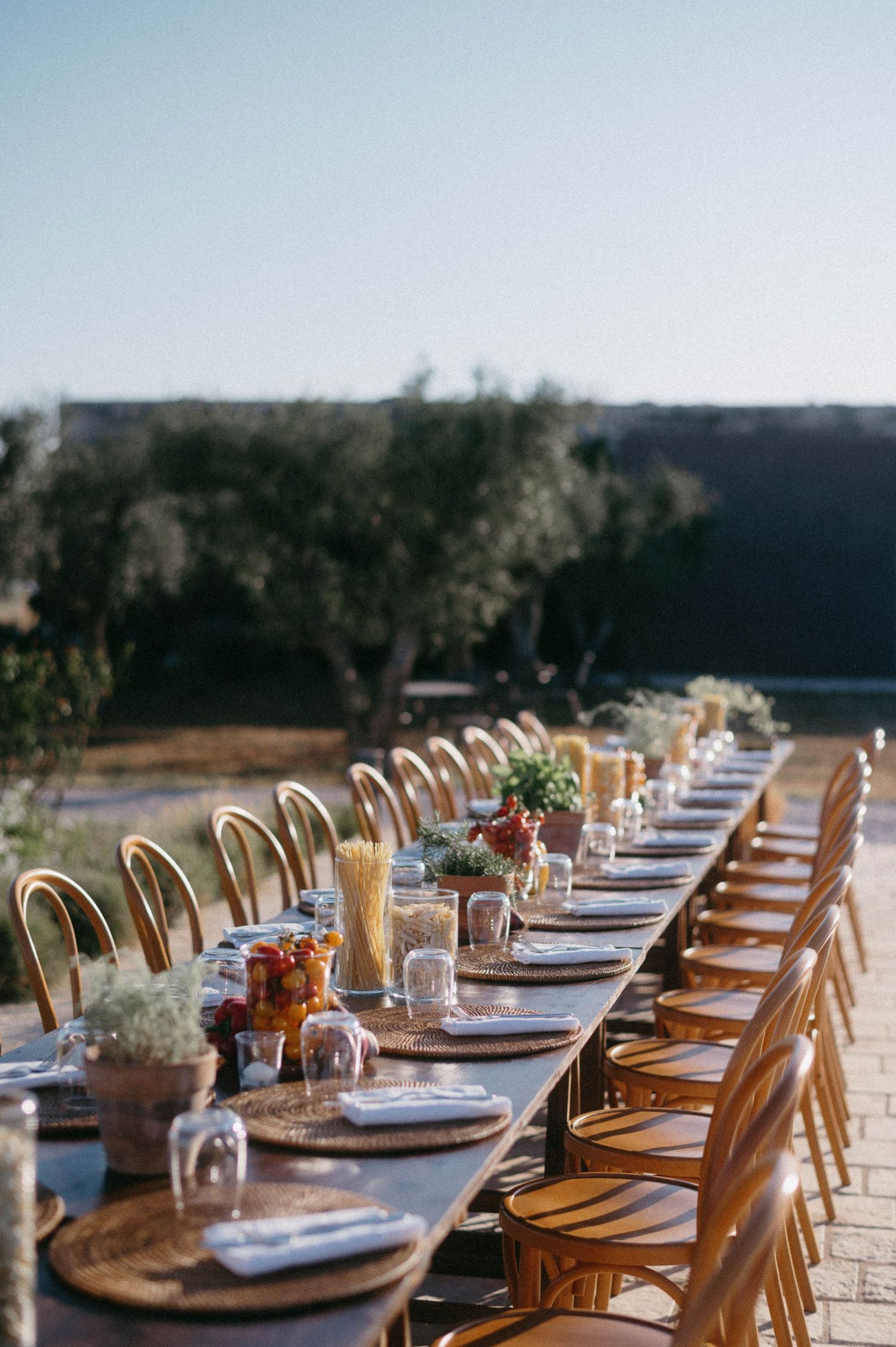 Elegant outdoor dining table setup with rattan chairs, white plates, and rustic decor for a wedding reception.