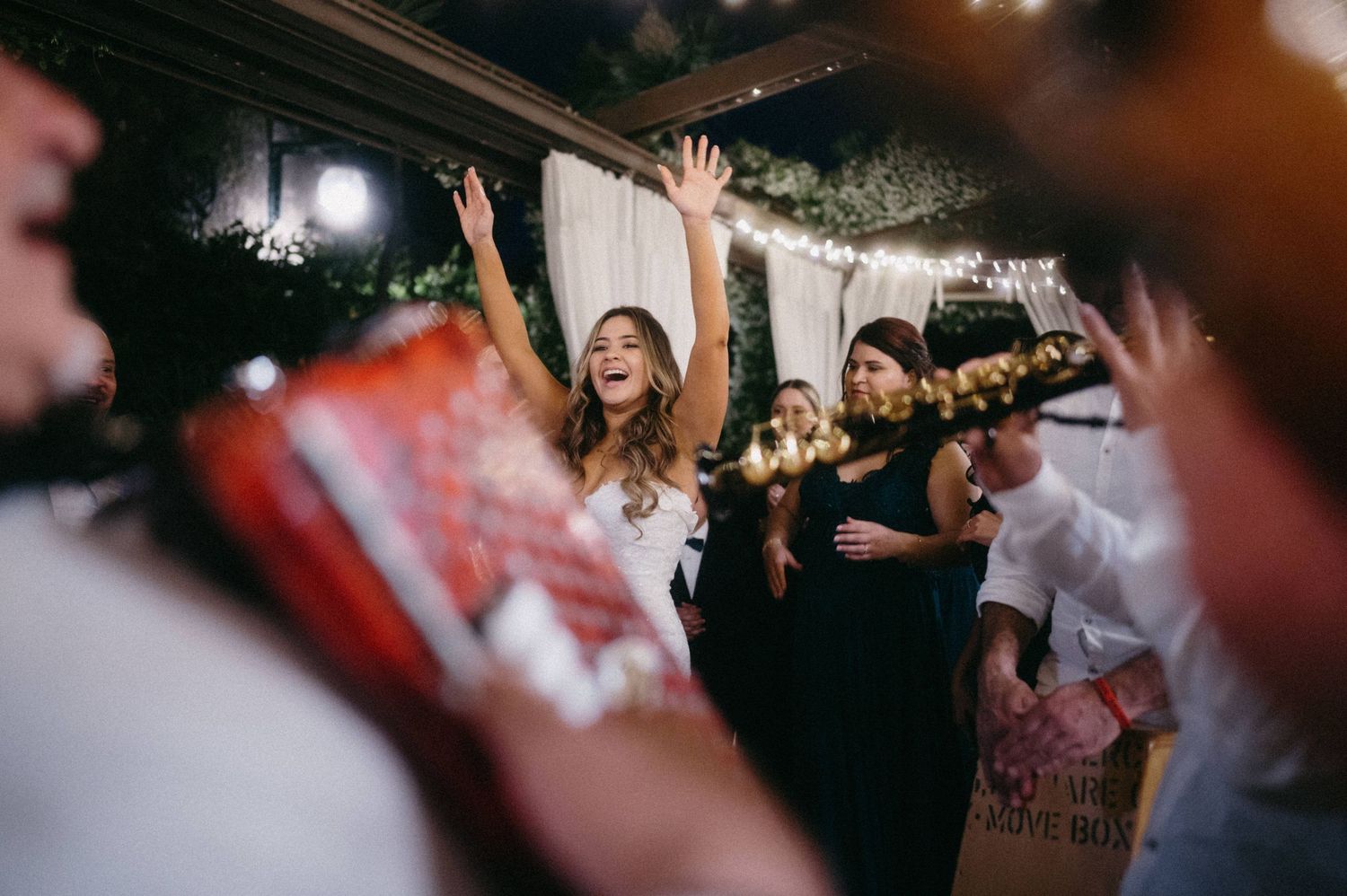 Energetic crowd dancing and celebrating with raised hands at a lively party under dim lighting.