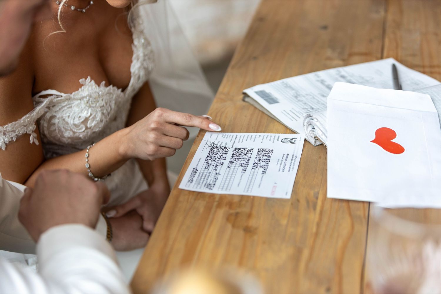 Bride points to wedding register document on wooden table during signing ceremony.