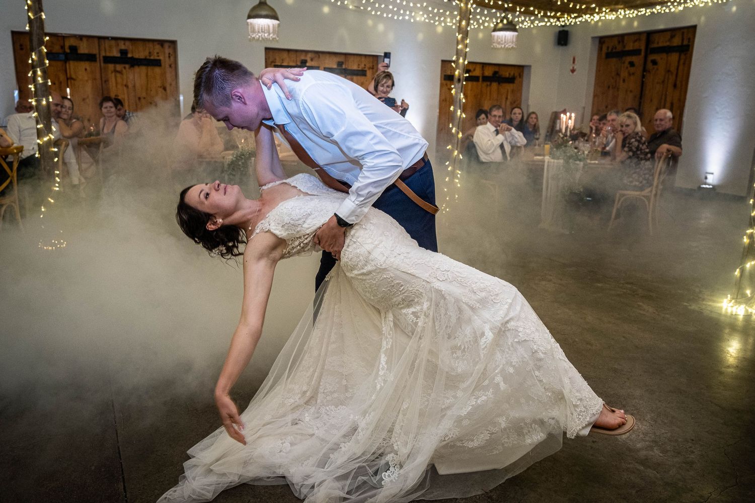 Groom dramatically dips bride on the dance floor surrounded by romantic fog at their wedding reception.