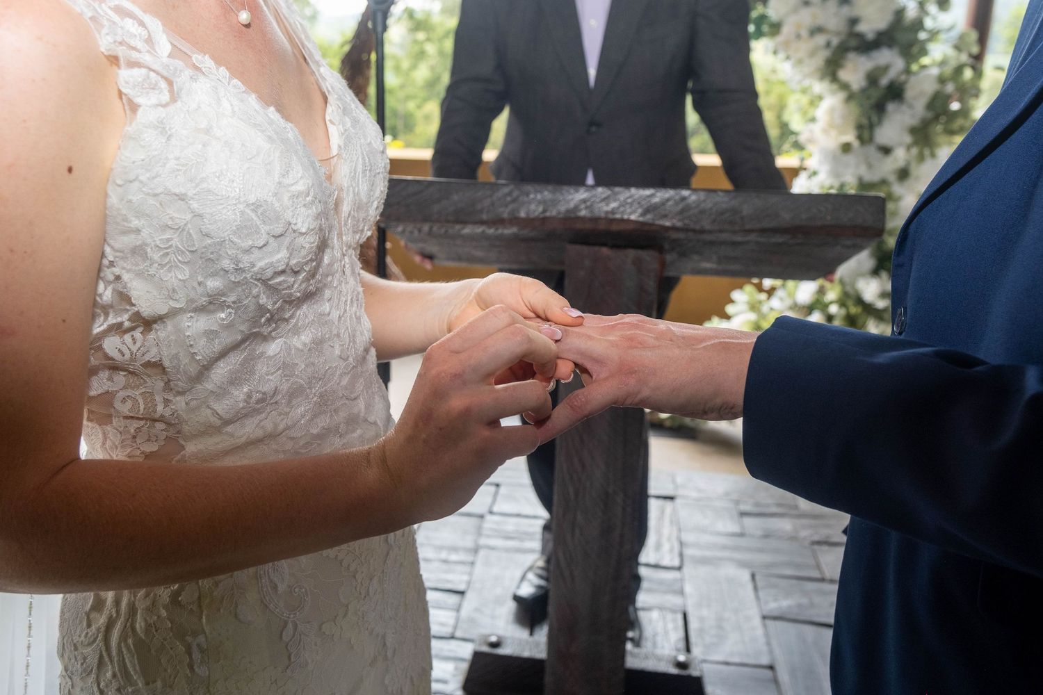 A bride places a gold wedding ring on the grooms finger during an outdoor wedding ceremony.