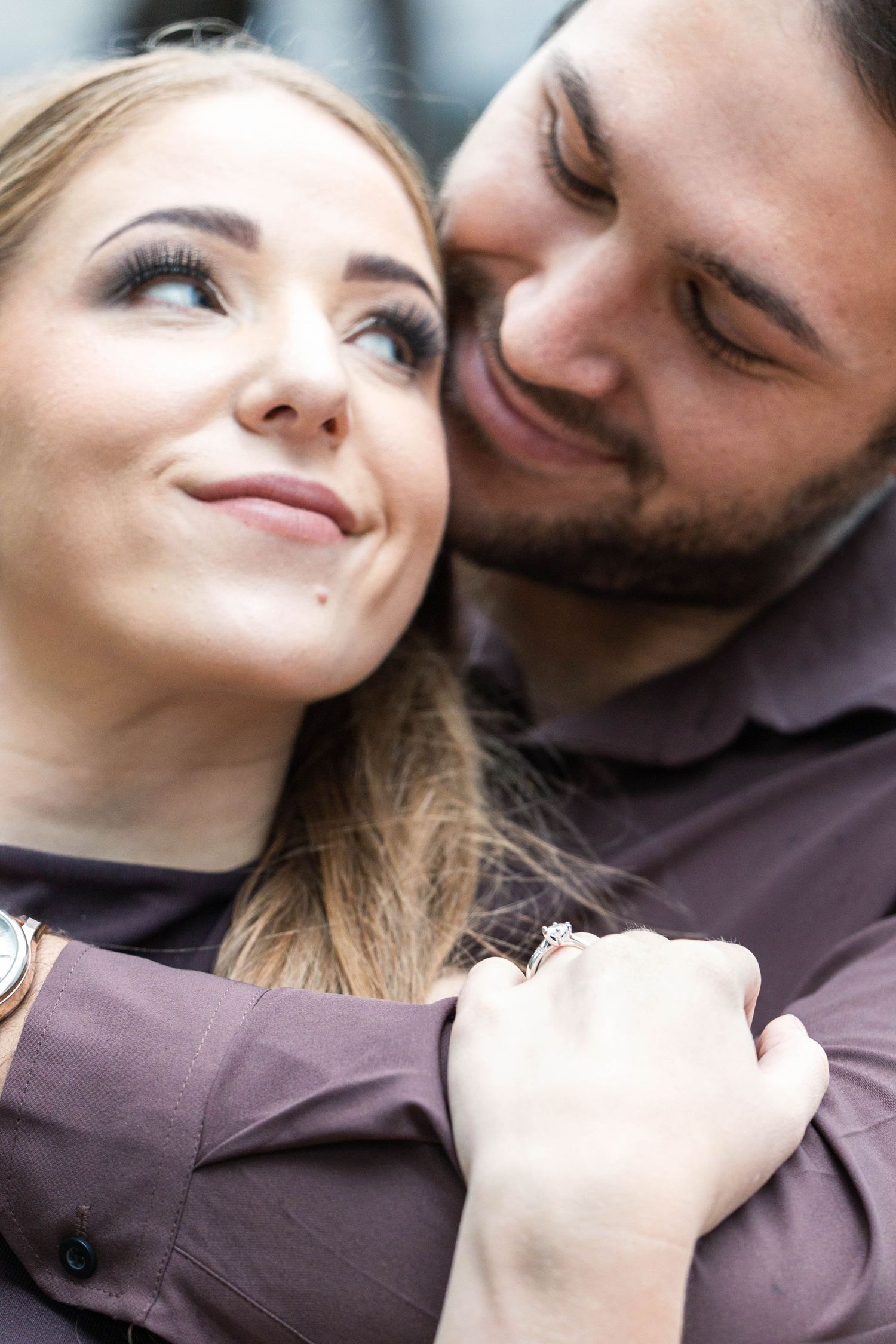 Romantic couple embracing closely, woman wearing an engagement ring, sharing a tender moment.
