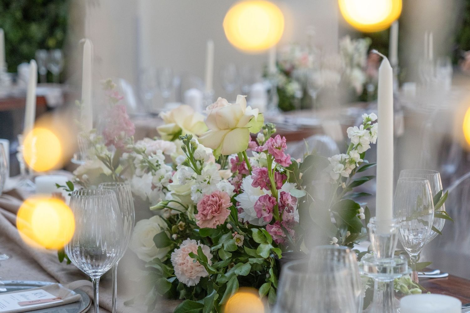 Elegant wedding table setting with pink and white floral centerpieces, candles, and crystal glassware.