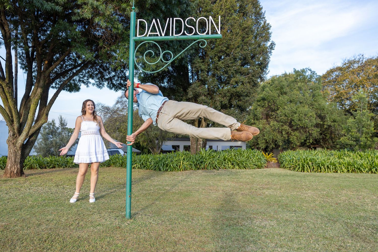 Groom to be performing a horizontal pole trick beside Davidson sign while woman in white dress watches.