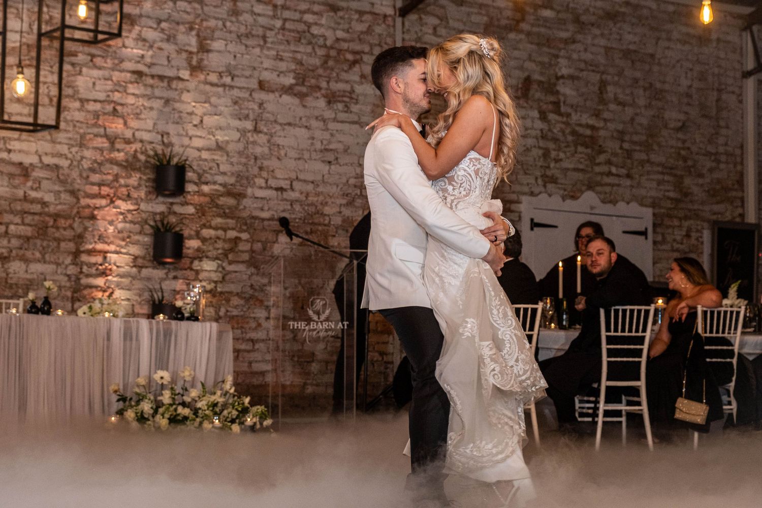 Bride and groom share romantic first dance surrounded by atmospheric fog at rustic barn wedding venue.