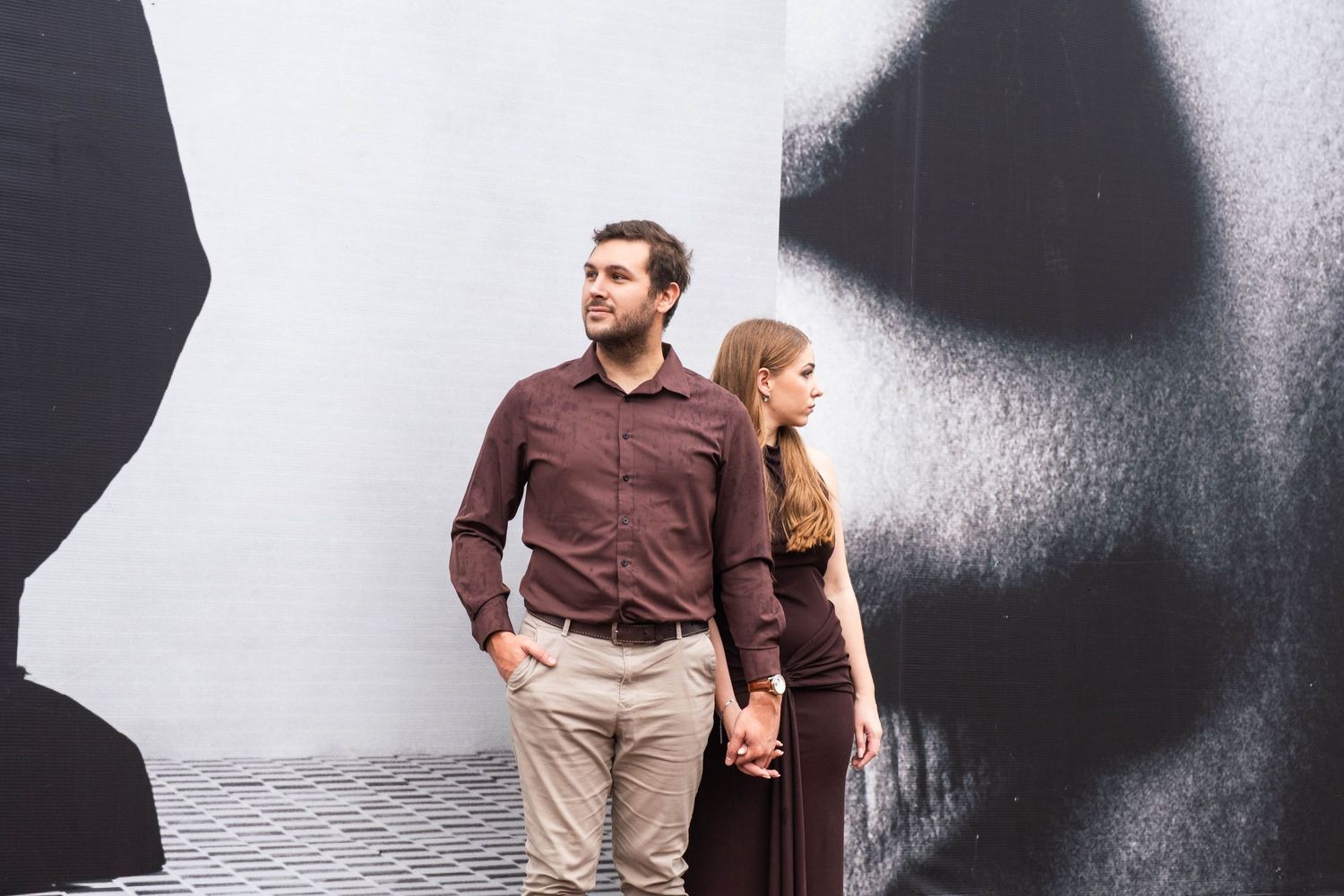 Couple holds hands while posing back-to-back against bold black and white urban street art mural wall.