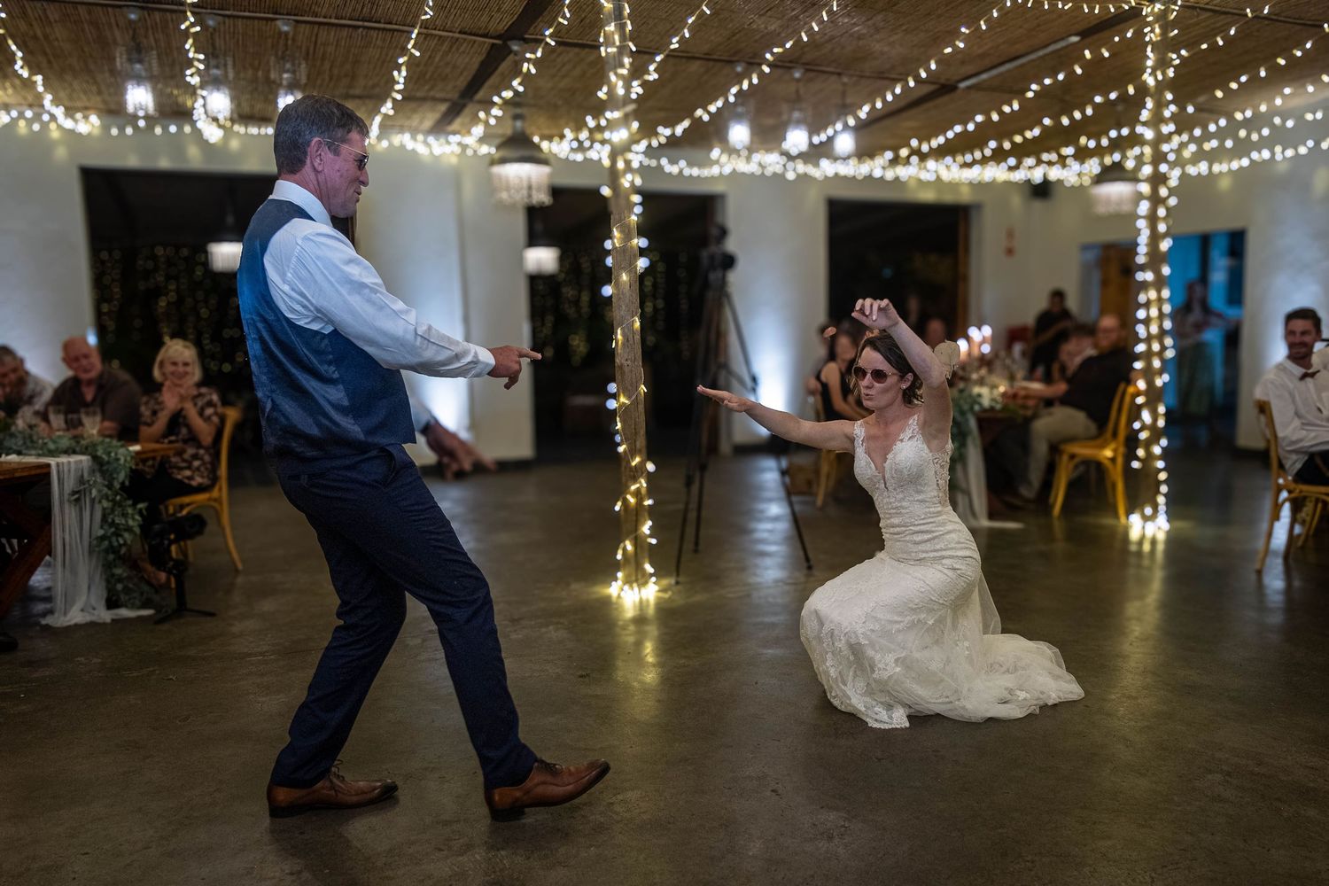Bride and groom performing an energetic first dance at a wedding reception with fairy lights.