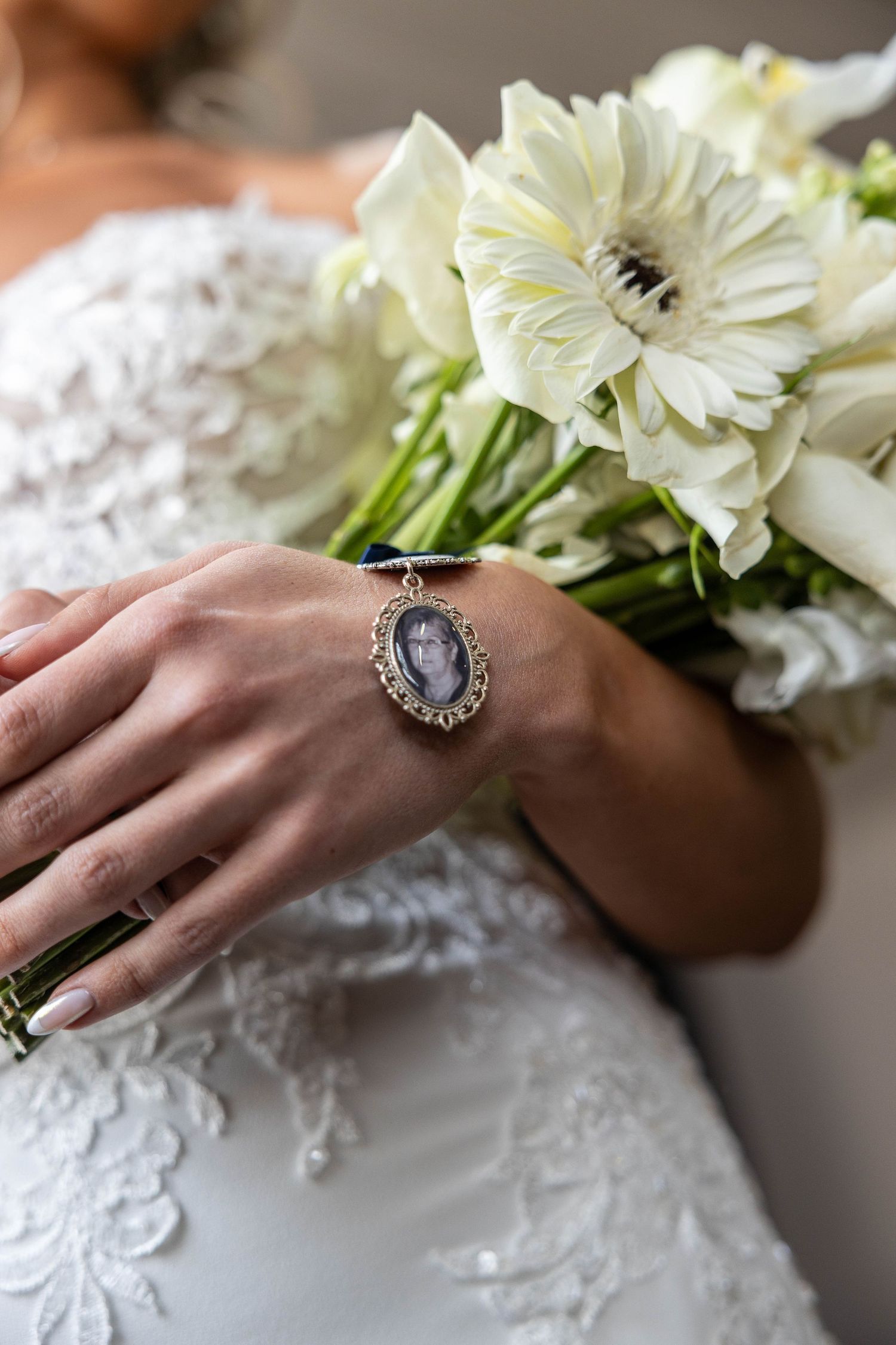 Close-up of bride holding white bouquet with a memorial photo locket charm on her wrist.