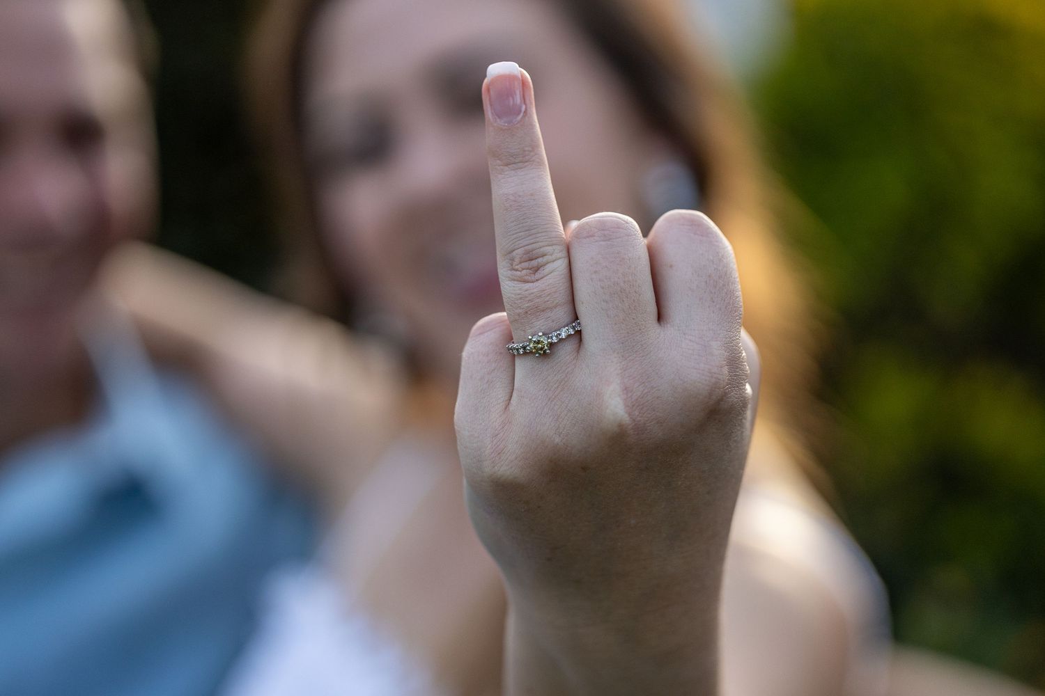Close-up of a woman showing off her engagement ring on her finger while smiling in a garden.