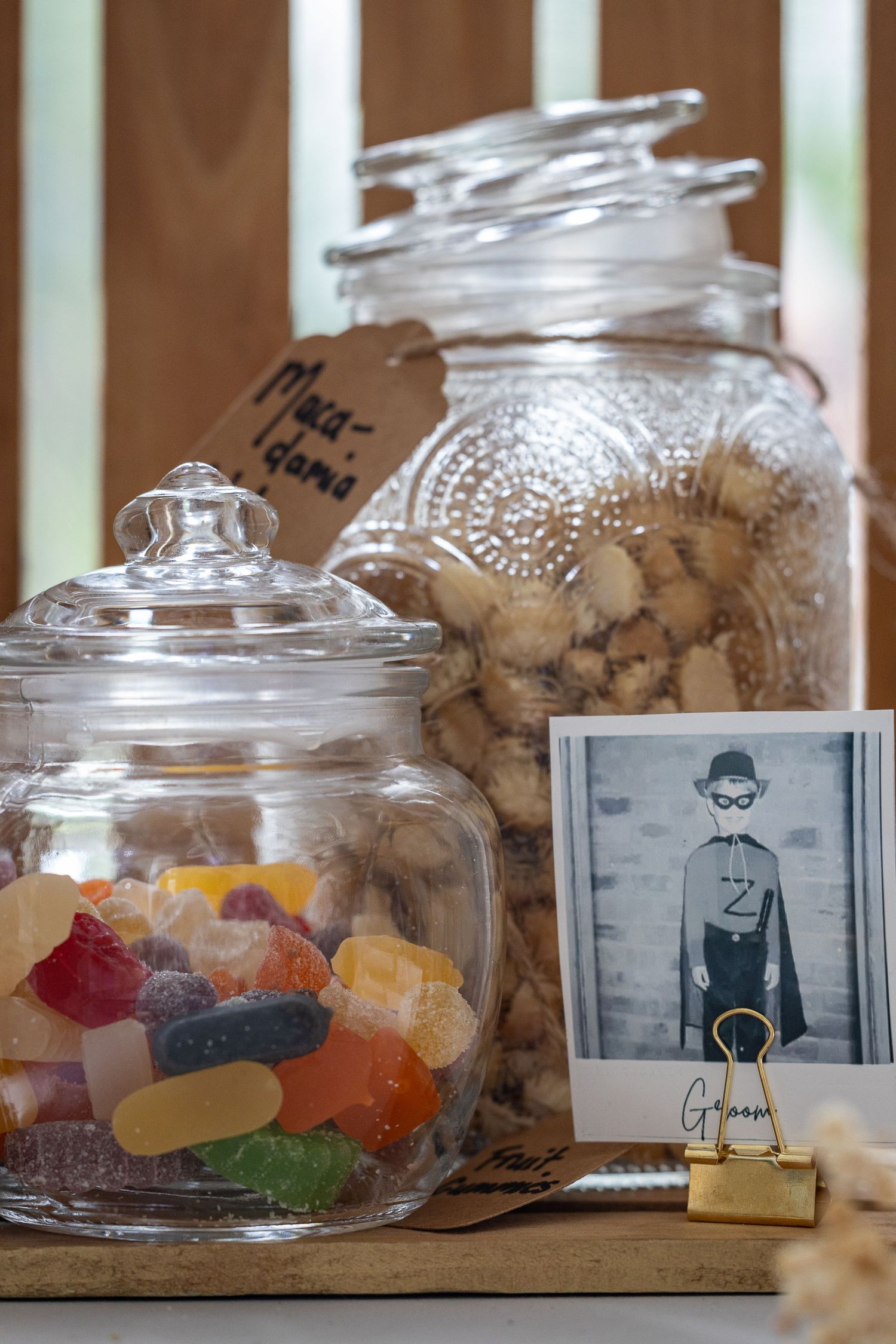 Glass jars filled with colorful gummy candies and macadamia nuts displayed on a wooden table at a wedding candy bar.