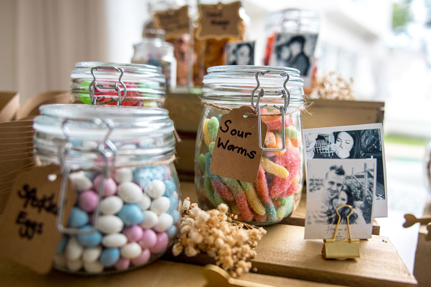 Colorful candy bar display with glass jars filled with sour worms and pastel sweets at wedding.