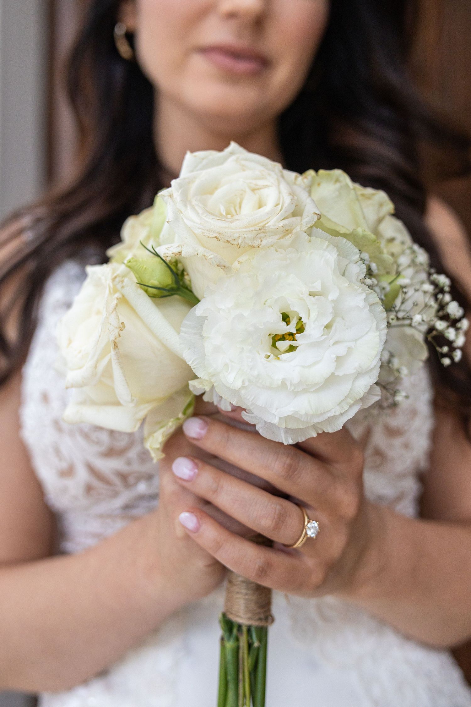 Bride in lace wedding dress holds elegant white rose and peony bouquet with gold engagement ring.