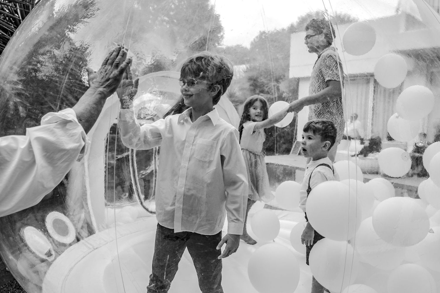 Black and white photo of children playing inside a large transparent balloon surrounded by white balloons.