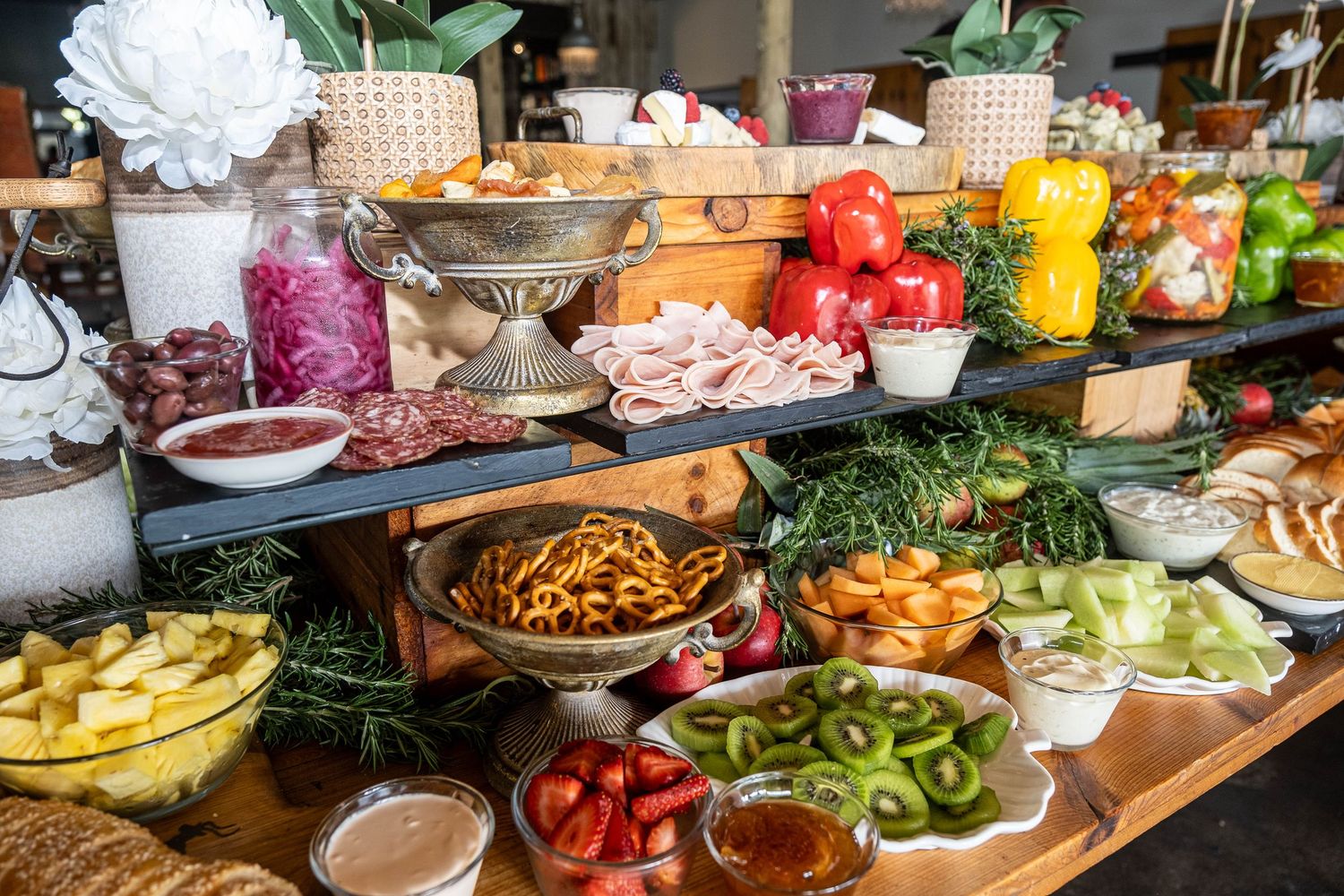 An elaborate wedding reception food buffet table filled with fresh fruits, vegetables, meats and snacks.