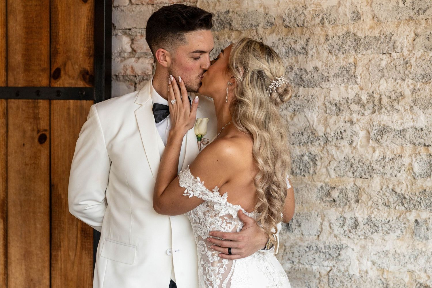 Bride and groom sharing a romantic kiss in rustic barn venue with exposed brick wall backdrop.