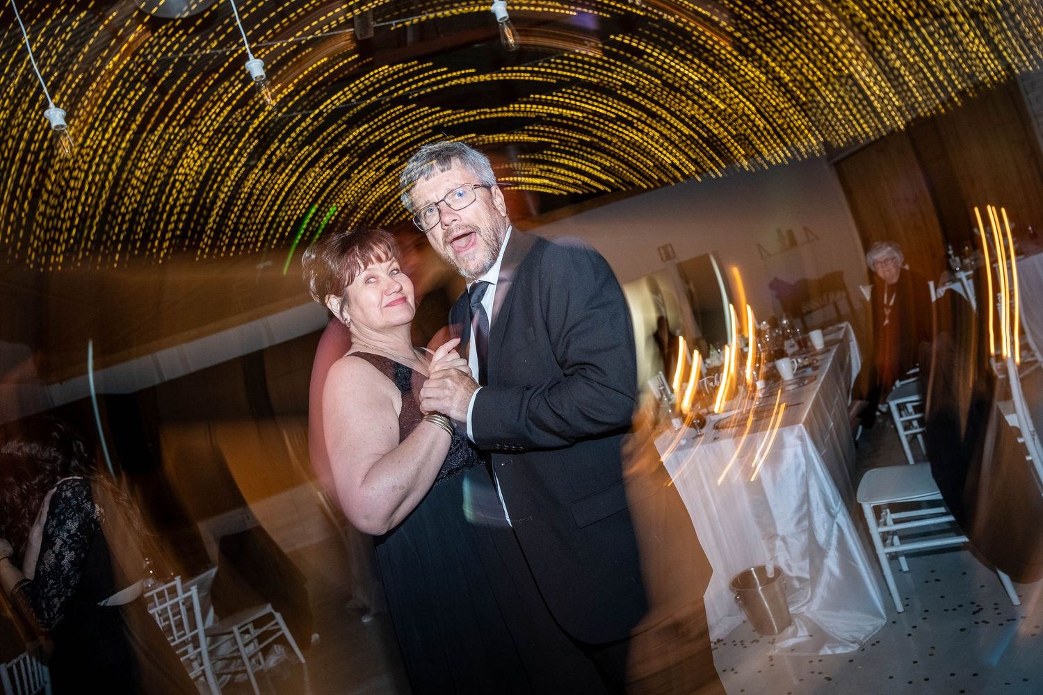 Couple slow dancing together under golden fairy lights at a romantic wedding reception.