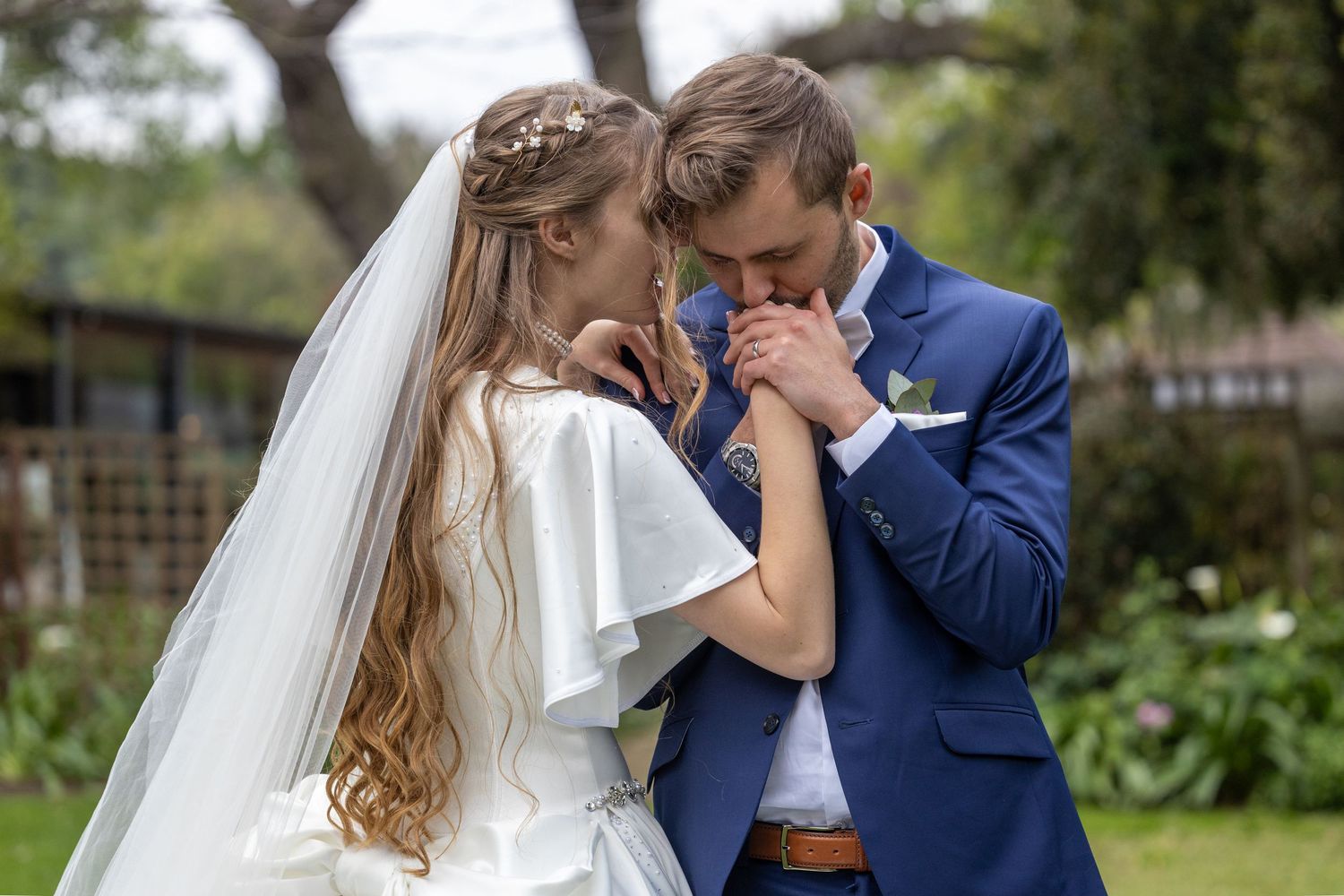 Groom kissing bride's hand tenderly in romantic outdoor wedding portrait.