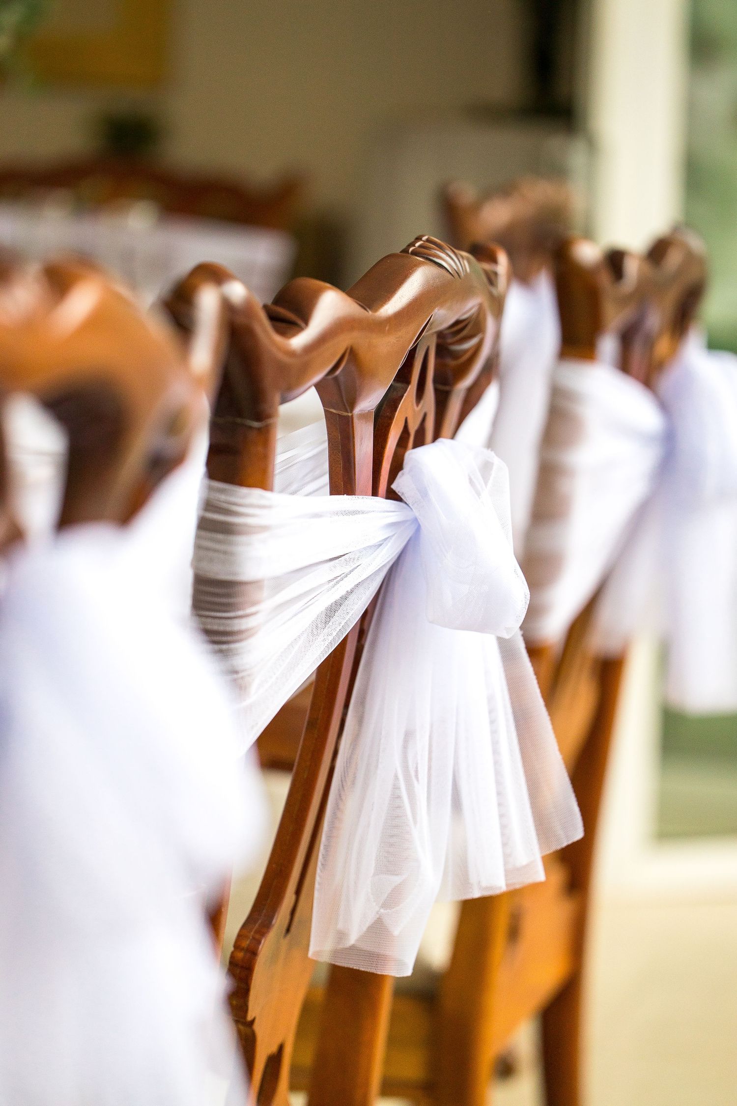 Elegant wooden wedding ceremony chairs decorated with white tulle ribbon bows in a row.