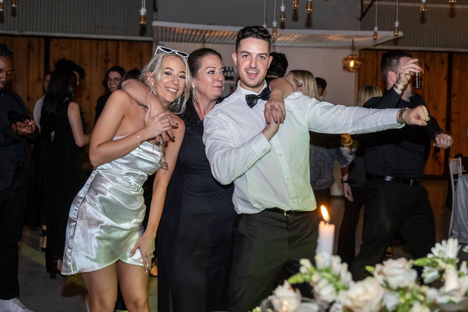 Two women and a man in bow tie posing and laughing together at a wedding reception.
