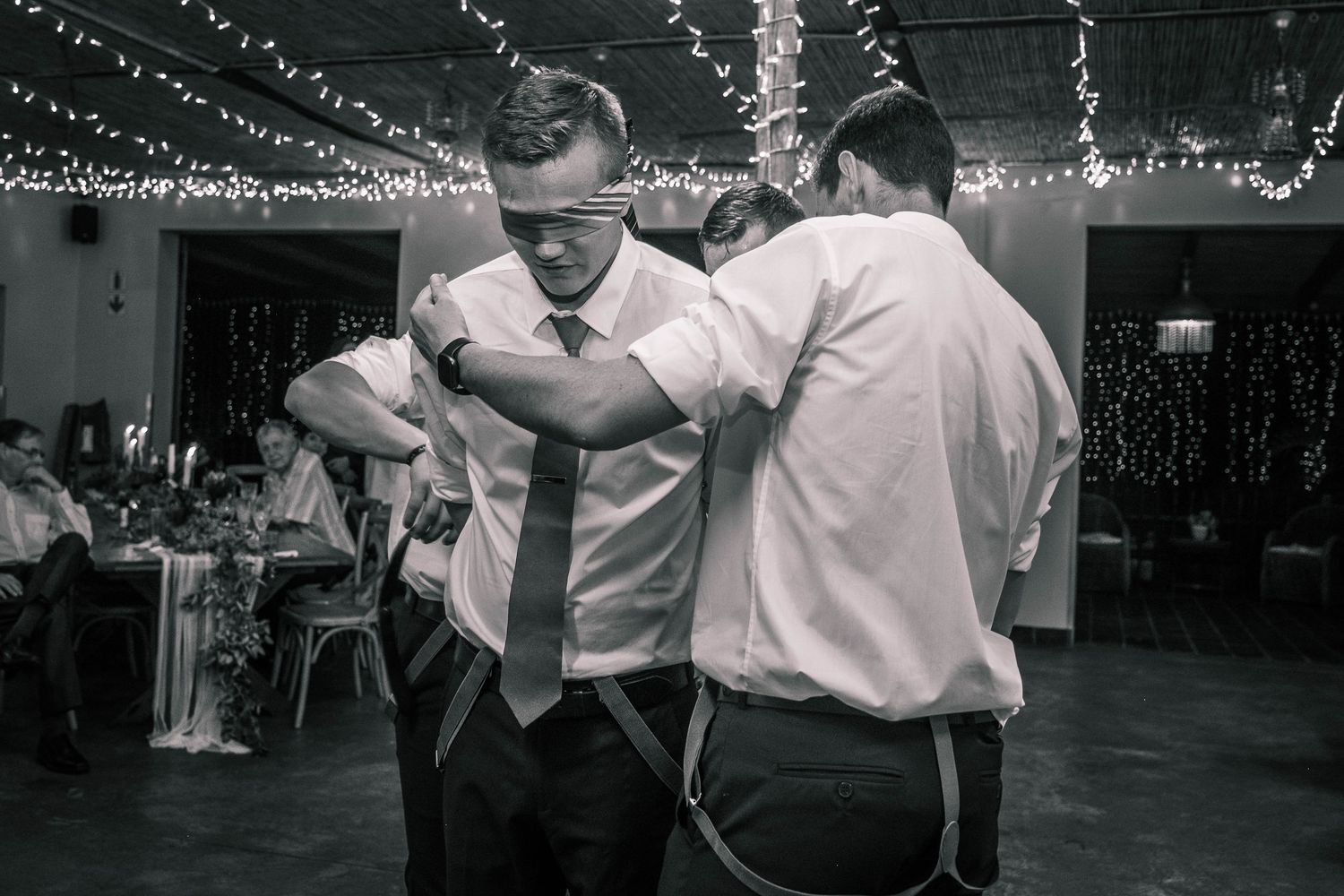 Groomsmen playfully tying up the groom on the dance floor at a wedding reception.