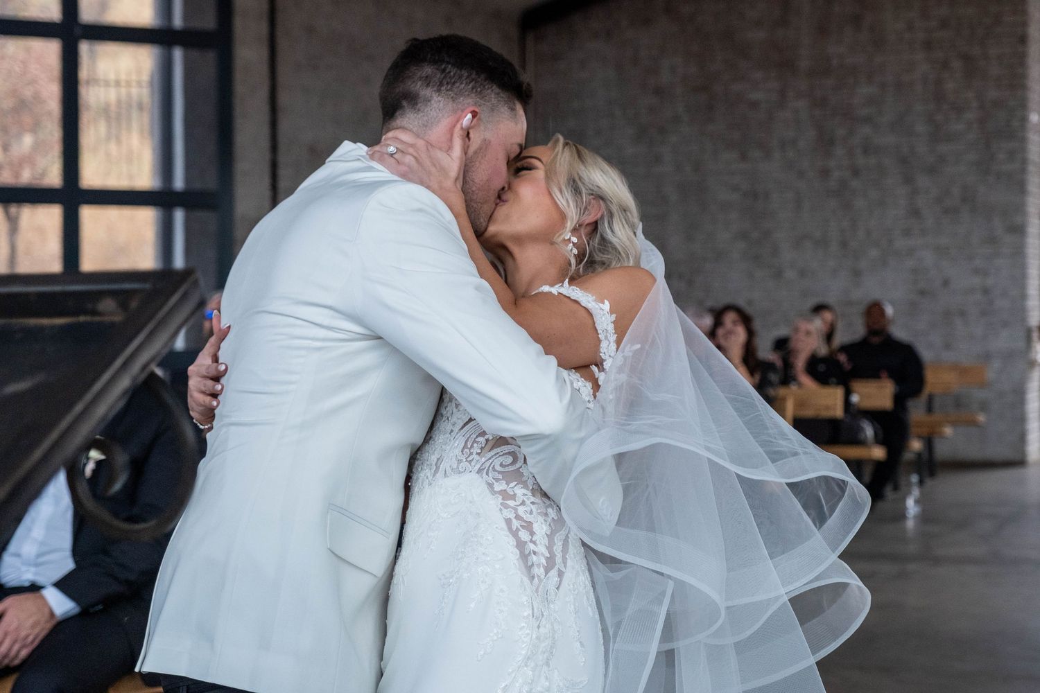 Newlyweds share first kiss as married couple during indoor wedding ceremony.