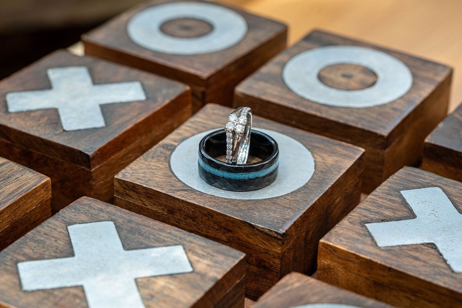 Wedding rings resting on a wooden tic-tac-toe game board with metal X and O inlays.