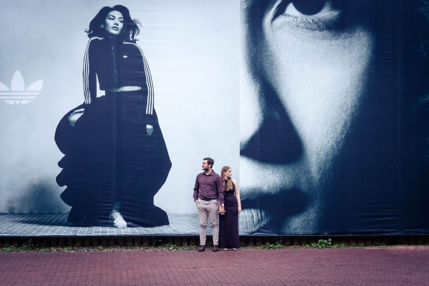 Couple posing in front of a large Adidas street mural artwork outdoors.