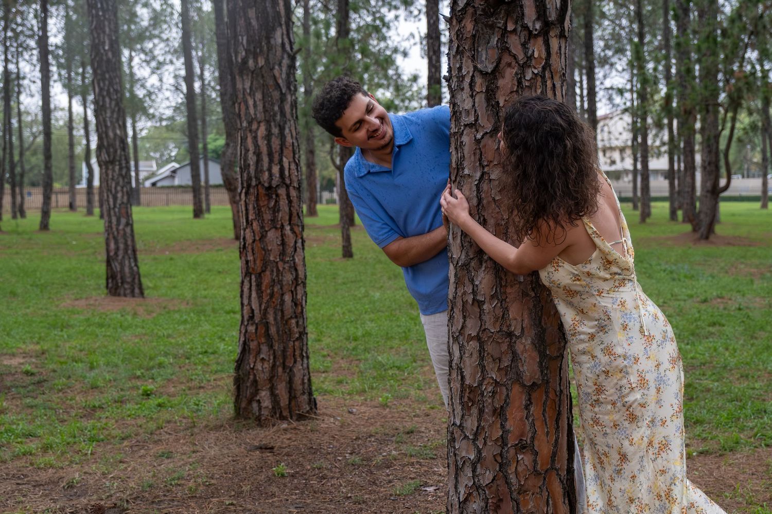 Playful couple peeking at each other from behind a tree in a park.