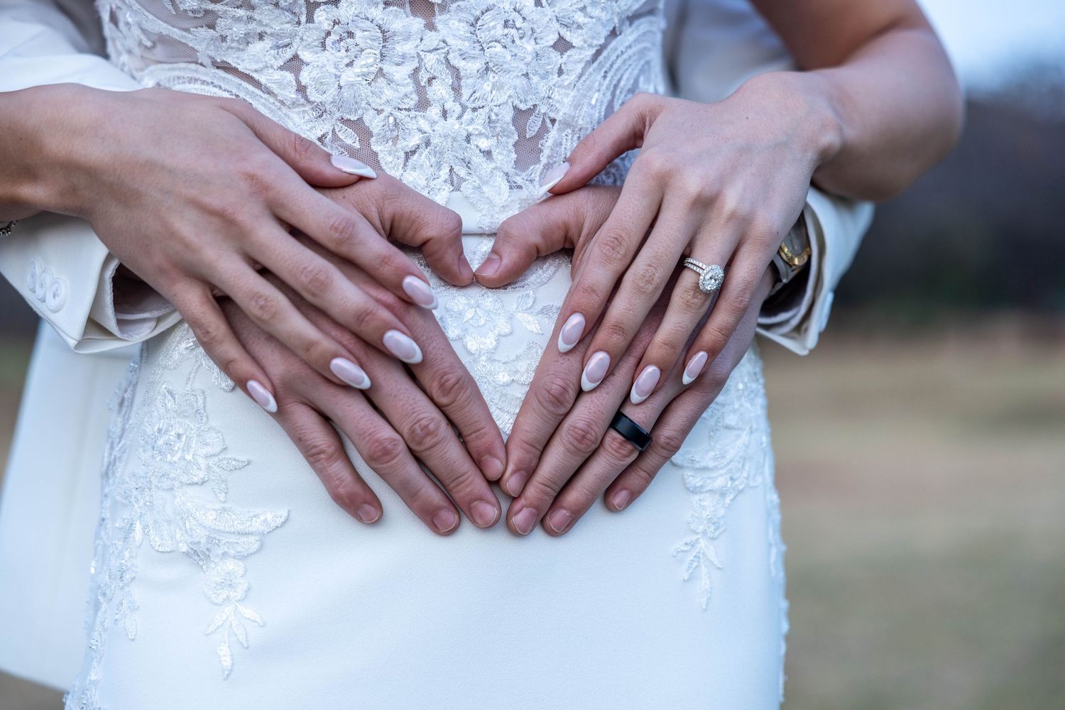 Bride and groom forming a heart shape with their hands on the bride's lace wedding dress.