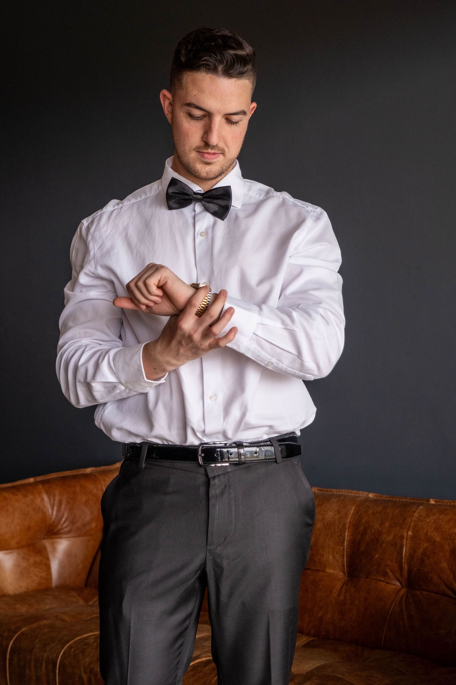 Dapper man in white shirt and bow tie fastening gold cufflinks.