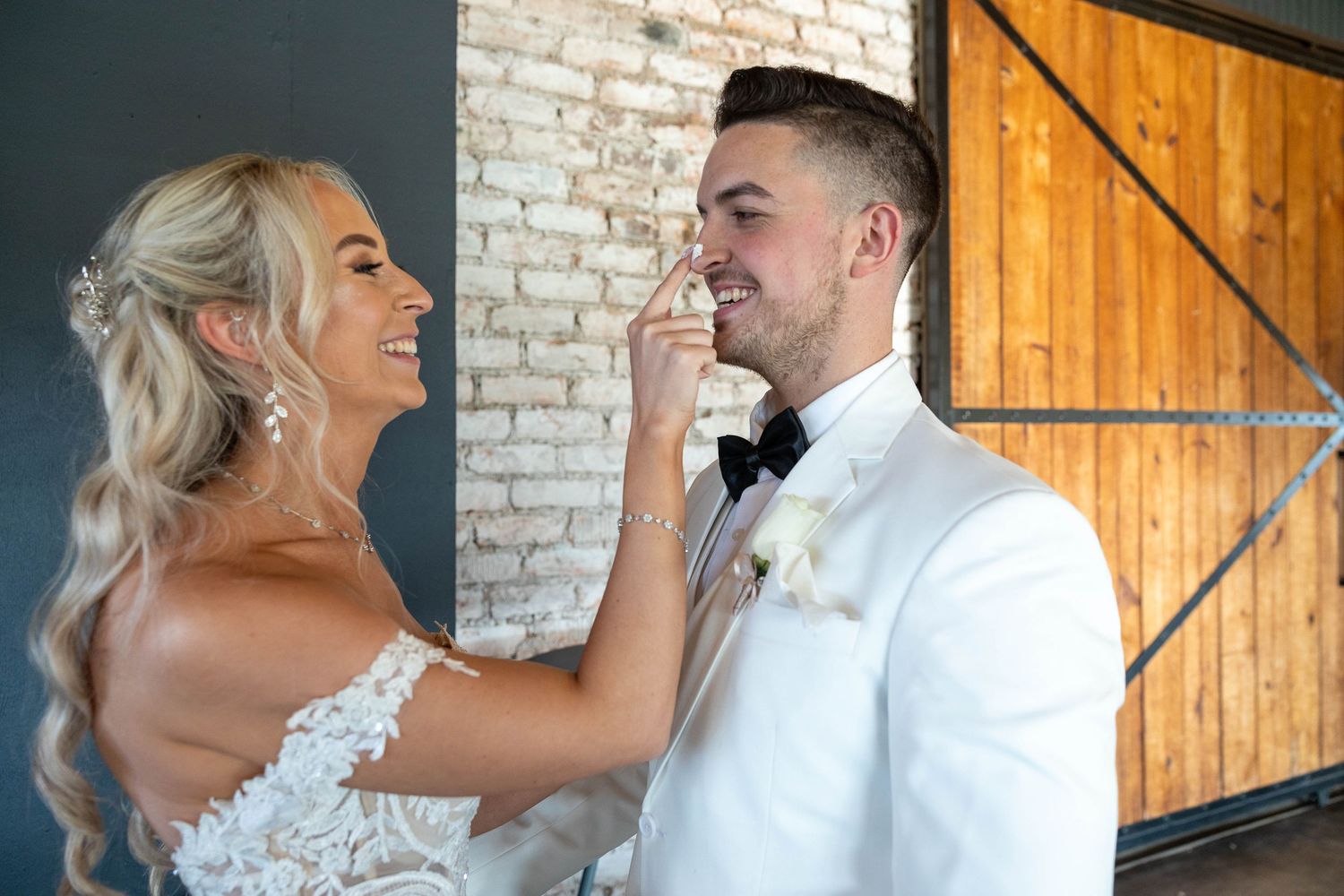 Bride in lace gown tenderly touching grooms face while sharing a joyful moment at wedding.