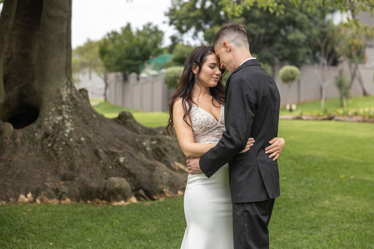 Bride and groom share a romantic embrace in a lush green garden during their wedding photo session.