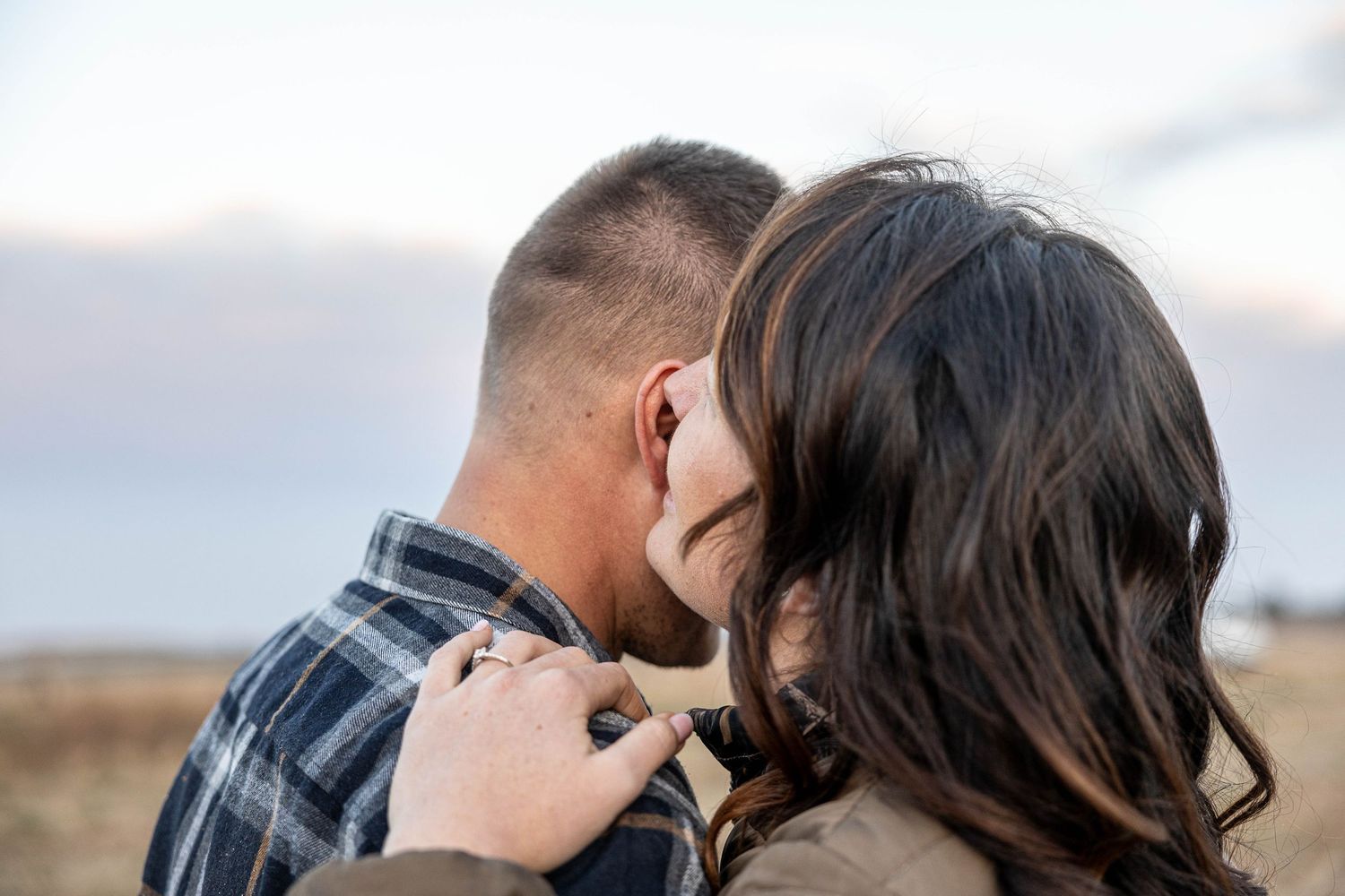Couple sharing an intimate moment outdoors, woman resting her head against man's cheek in a romantic embrace.