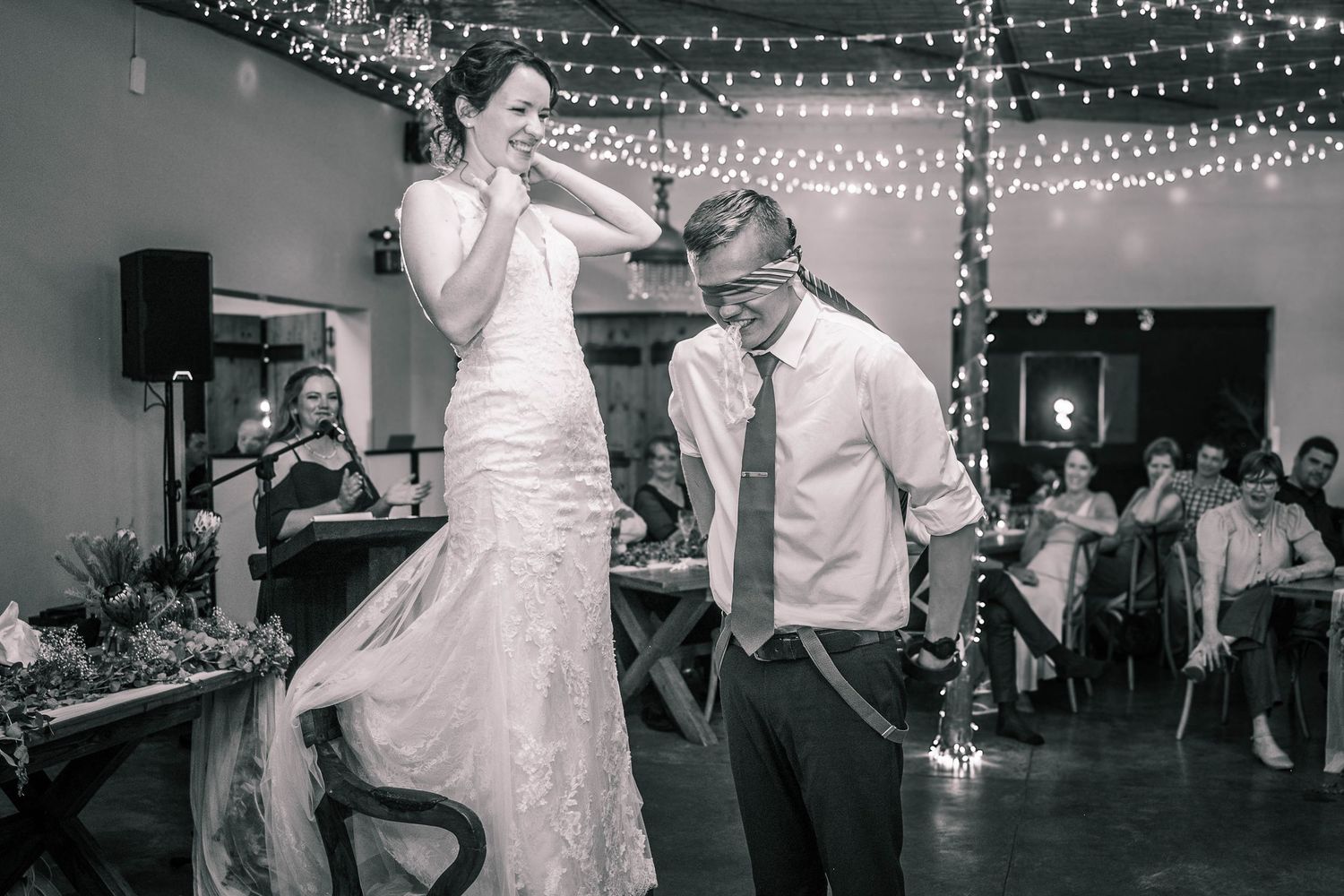 Bride dancing with groom under fairy lights at a wedding reception in black and white.
