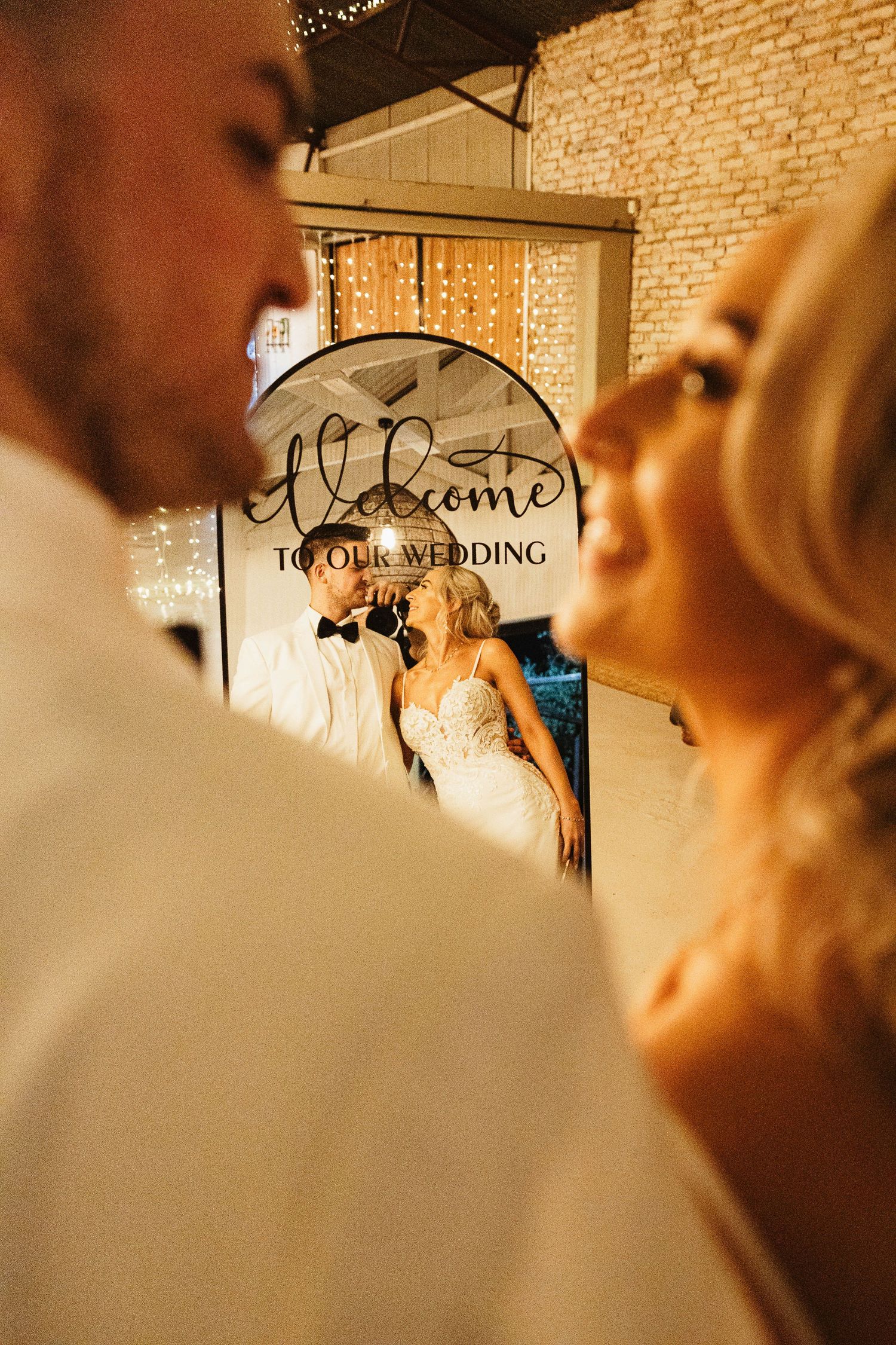 Newlyweds reflected in welcome mirror sign at elegant rustic wedding reception venue.