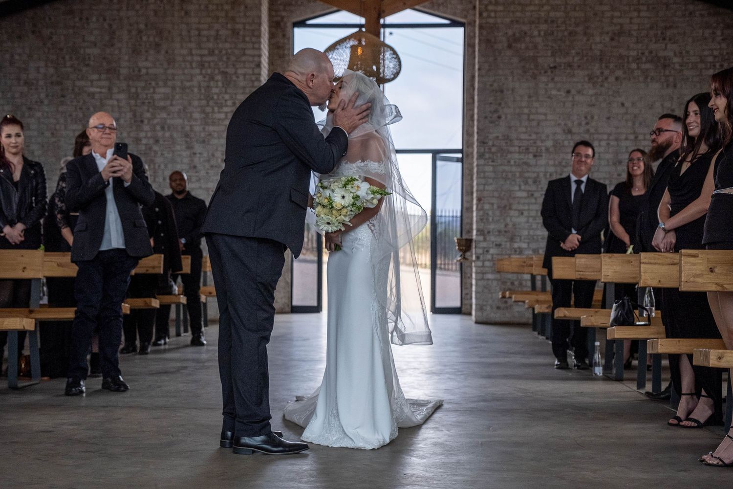 A father shares a tender kiss with his daughter the bride in a white gown at the wedding ceremony altar.