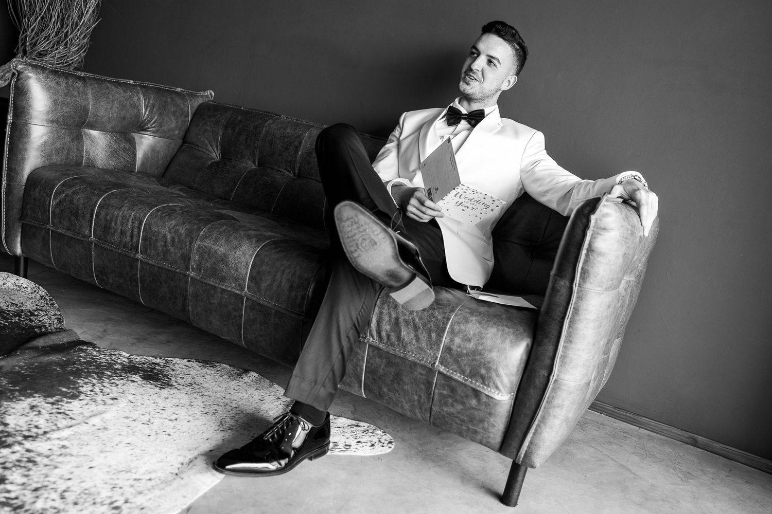 Black and white portrait of stylish man relaxing on leather sofa in bow tie.