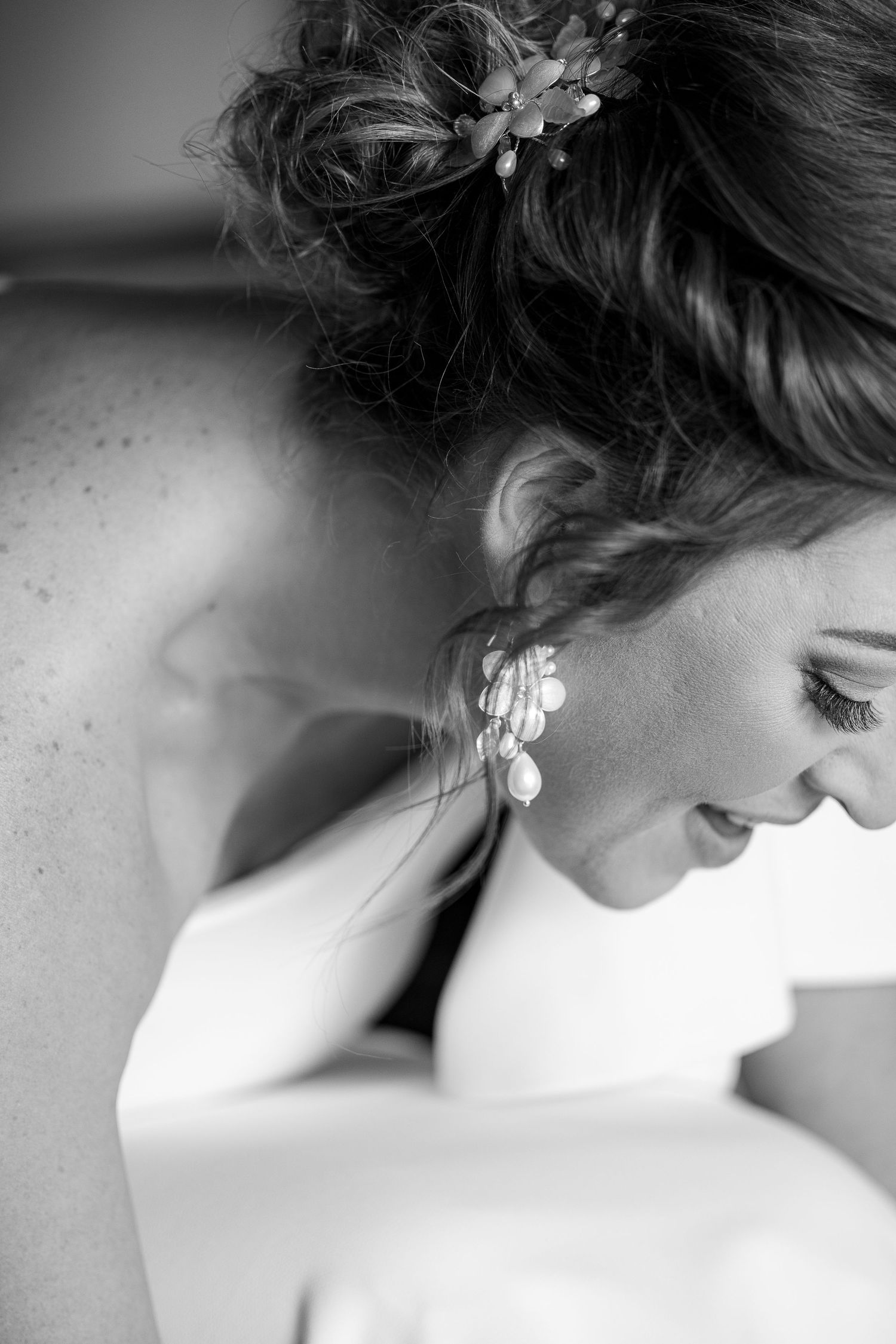 Black and white portrait of smiling bride with updo hairstyle adorned with flowers and dangling earrings.