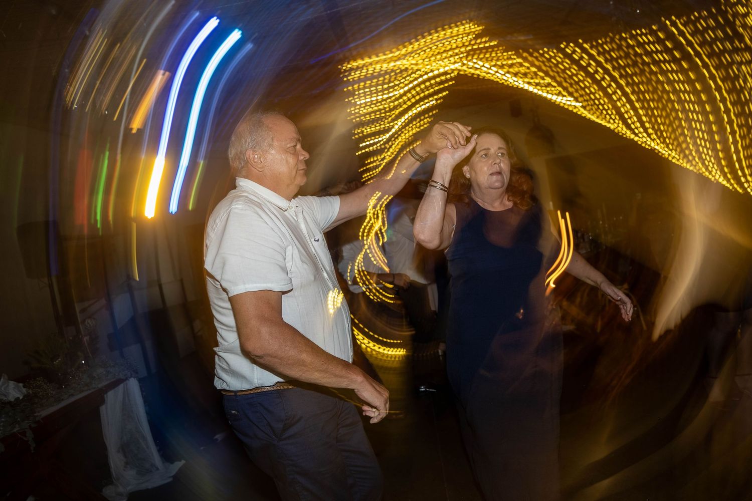 Couple dancing energetically with swirling colorful lights at a festive wedding reception.