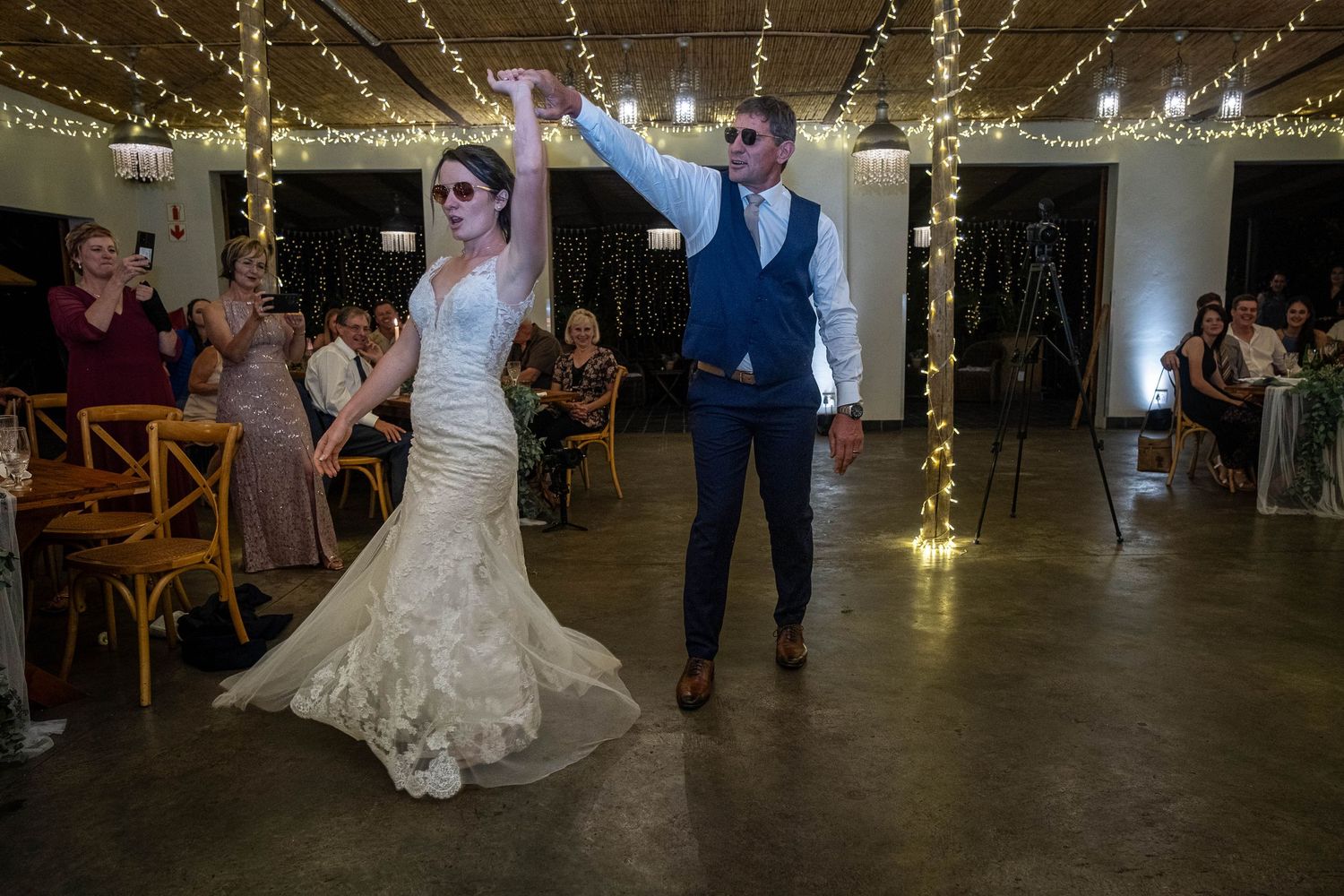 Bride and groom sharing a celebratory first dance under fairy lights at wedding reception.