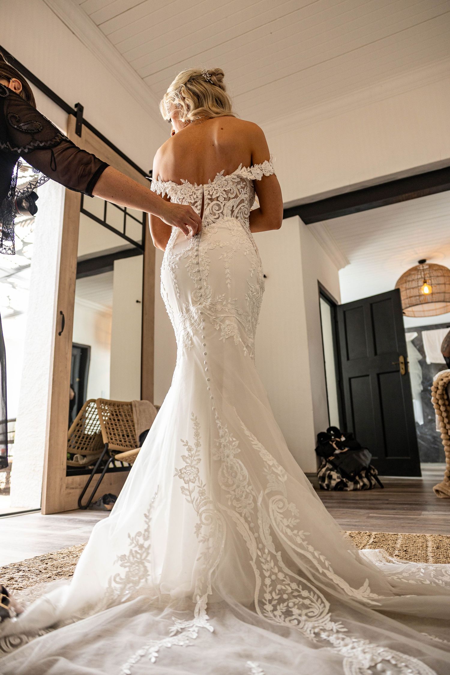 Back view of bride in fitted lace mermaid wedding gown with long train being buttoned.