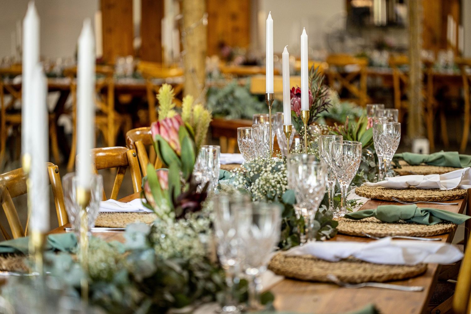 Elegant rustic wedding reception table with white candles, crystal glasses, green napkins, and tropical floral centerpieces.