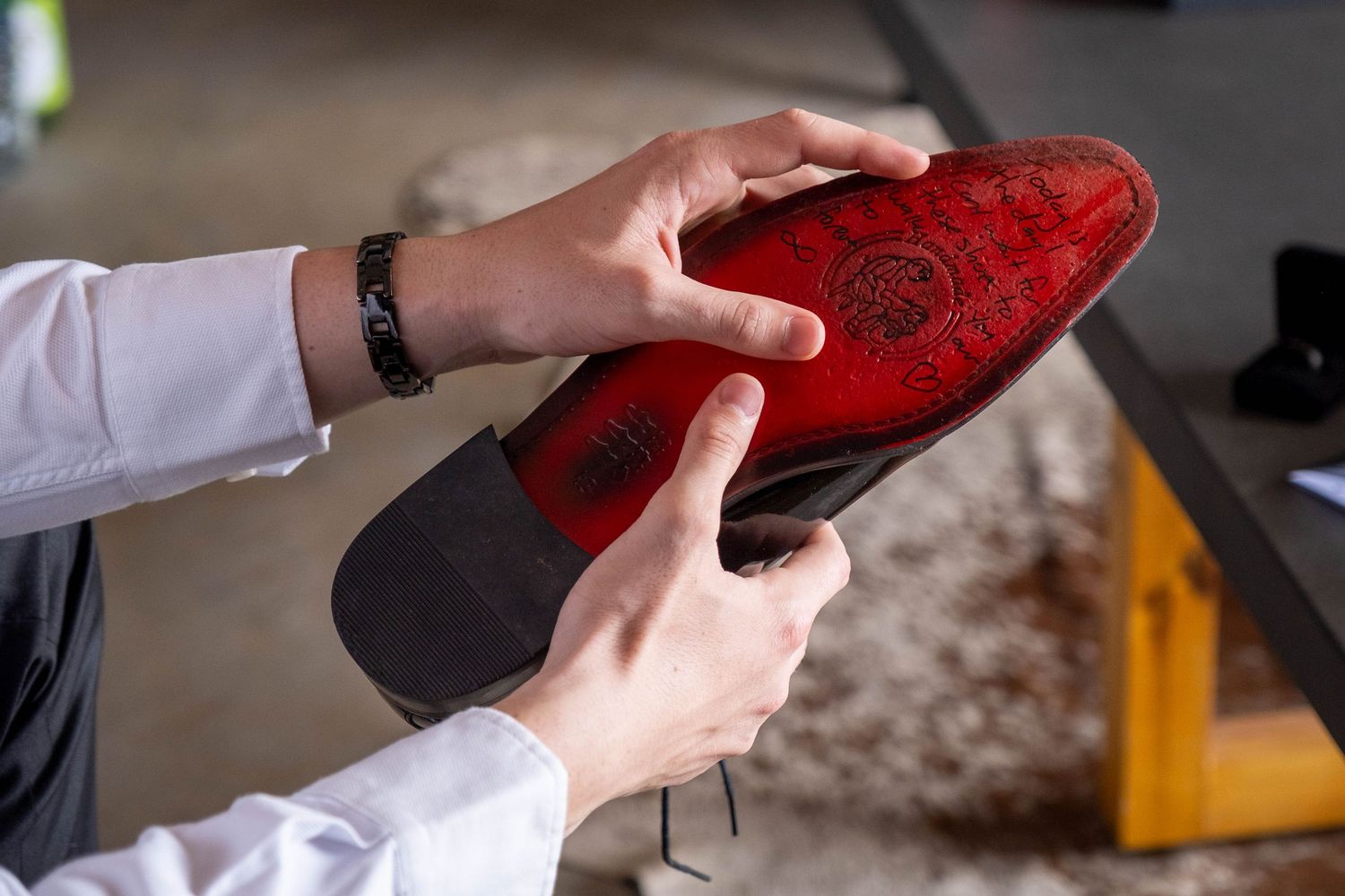 Close-up of hands holding a red-soled luxury dress shoe, examining the branded sole.