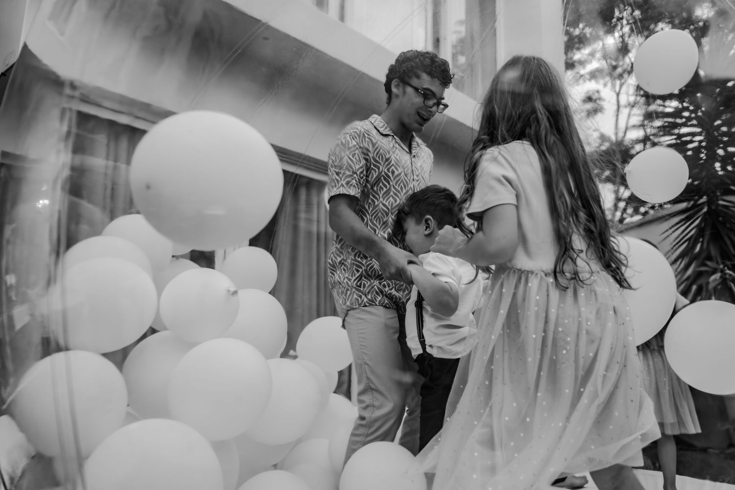 Black and white photo of a man and two children playing among large white balloons at an outdoor event.