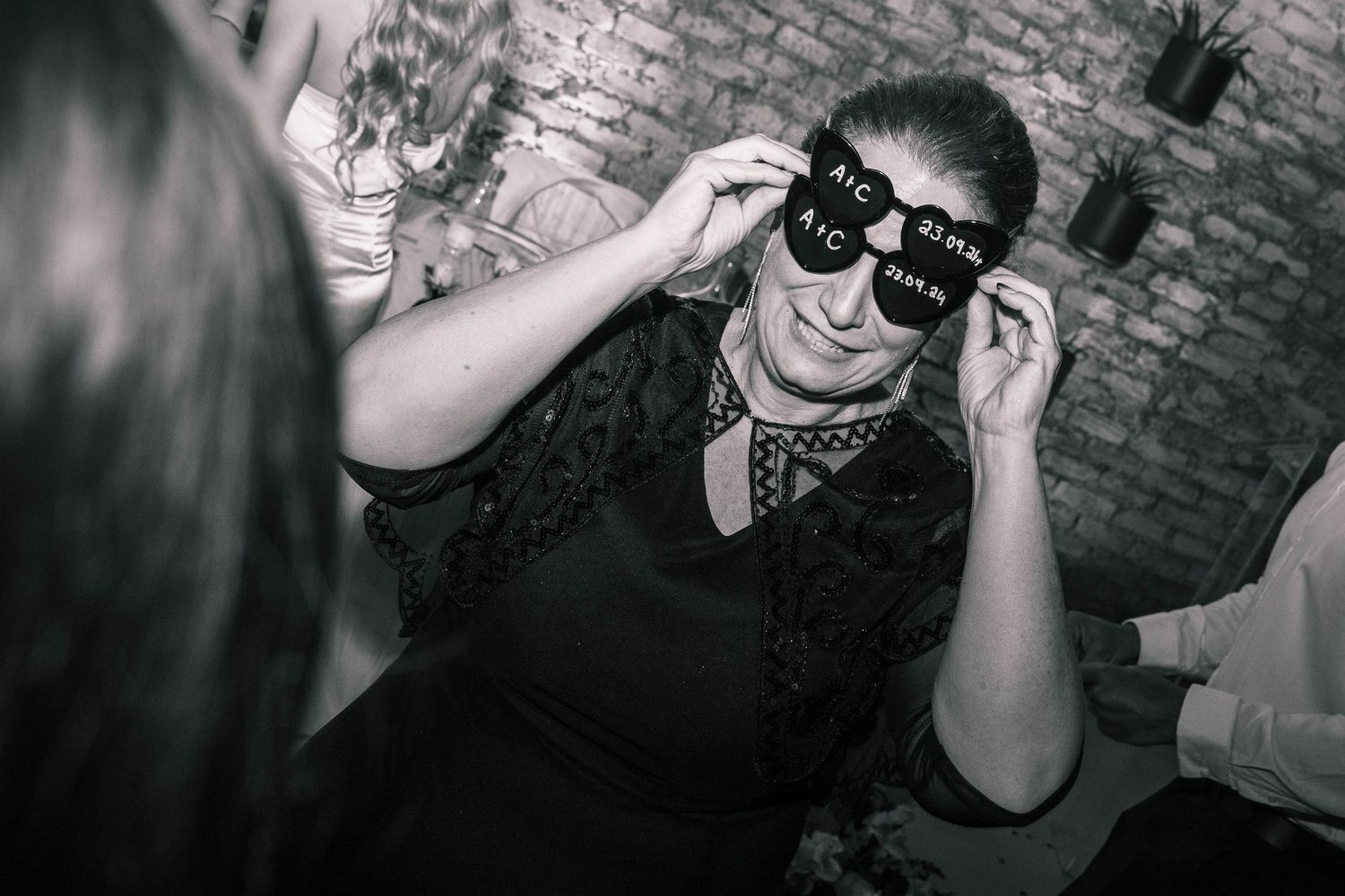 Black and white photo of a woman wearing novelty wedding party sunglasses at a reception.
